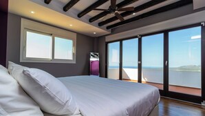 Un dormitorio con una cama grande, un ventilador de techo y vistas al mar a través de una puerta corrediza de vidrio.