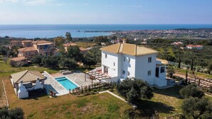 Una villa blanca con piscina, rodeada de olivos y vistas al mar.