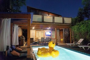 Guests can enjoy a refreshing swim in the pool surrounded by lush greenery and a wooden deck.