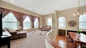 A spacious living room with a curved wooden floor, a sofa set, a dining table, and a large window with patterned curtains.