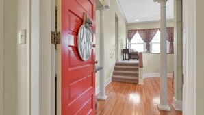 A hallway with a red door, wooden flooring, and white columns.