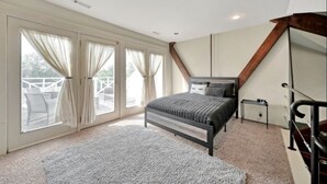 A bedroom with a large bed, a desk, and a view through a sliding glass door to an outdoor area.