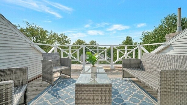 An outdoor patio with wicker furniture, a central table, and a white railing.