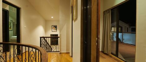 Un pasillo con piso de madera, una escalera con barandilla negra y una puerta que da a un balcón.