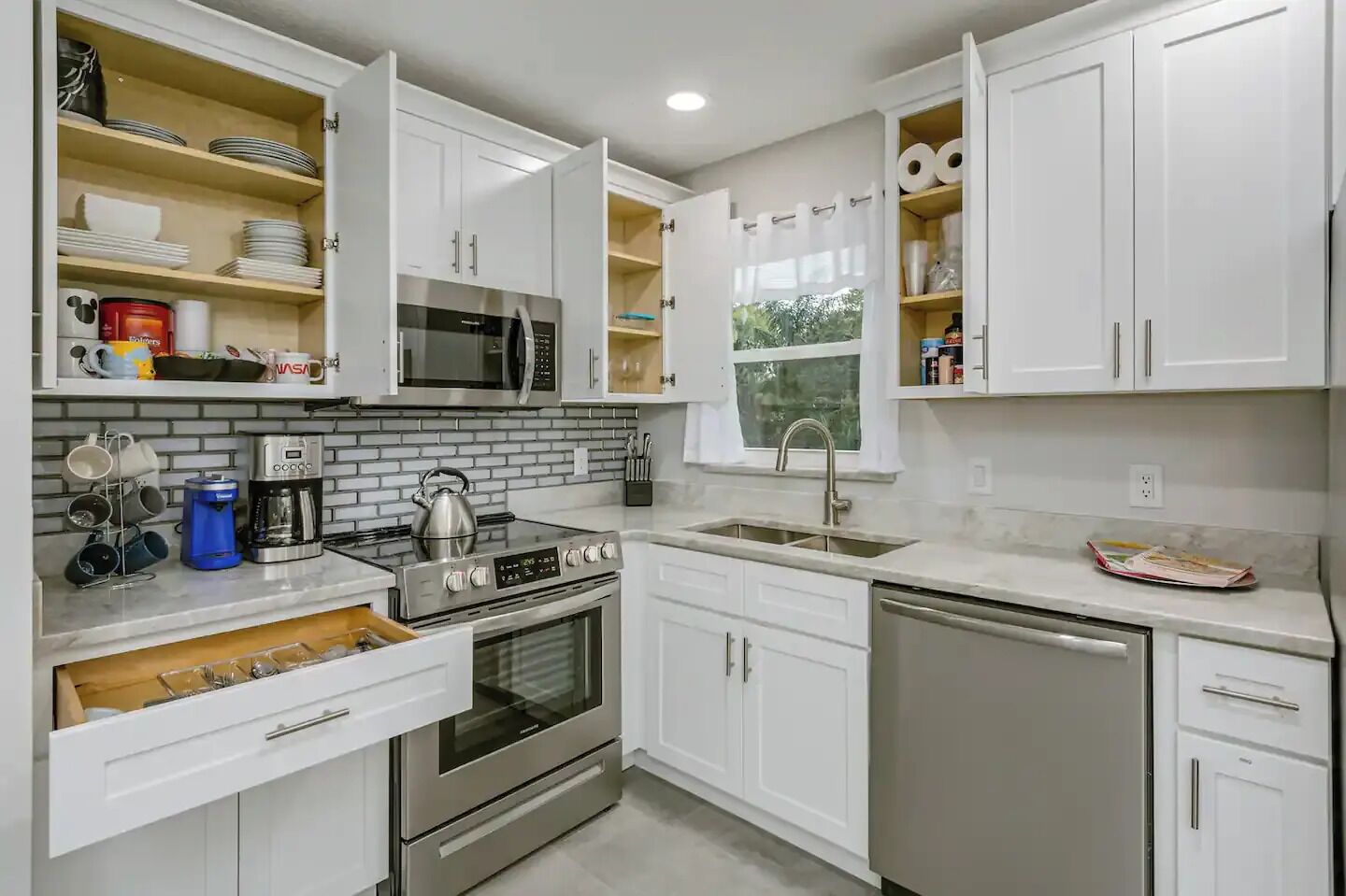 A modern kitchen with white cabinets, a stainless steel stove, a microwave, and a dishwasher.