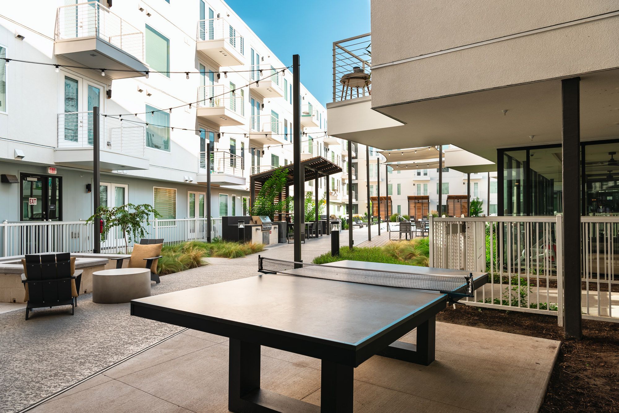 Un patio al aire libre con mesa de ping pong, mobiliario y una parrilla.