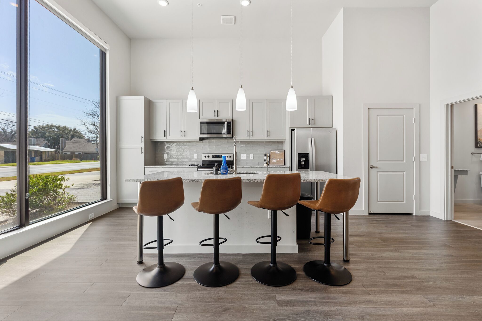 Una cocina moderna con armarios blancos, una isla central con taburetes, un ventanal y vistas al exterior.