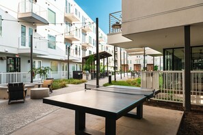 Ein Außenbereich mit Terrasse, einem Tischtennisch, Sitzgelegenheiten und einem Grill.