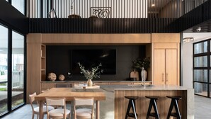 Een moderne keuken met een grote televisie, houten keukenkastjes en een bar voorzien van krukken.