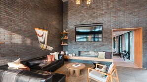 Een moderne woonkamer met een bakstenen muur, een leren bank, een houten salontafel en een flatscreen televisie boven een open haard.