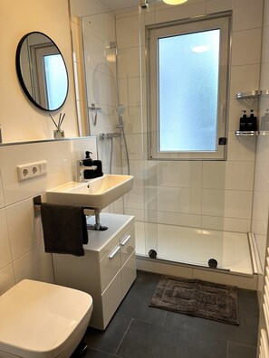 A modern bathroom with a toilet, sink, mirror, shower, and a window. - RtR Essen (Essen)