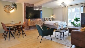 Ein modernes Wohnzimmer mit Kamin aus Backsteinen, einem großen Flachbildfernseher, einem Essbereich mit Holztisch und -stühlen sowie einem gemütlichen Bett mit Stadtblick.