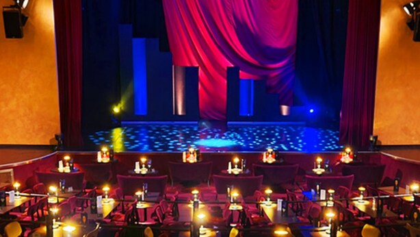 Ein Theater mit Bühne, roten Vorhängen und Tischen mit Kerzen.