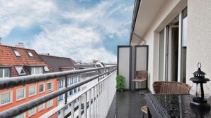 Ein Balkon mit Blick auf angrenzende Gebäude, eine kleine Sitzecke mit Stühlen und ein Blumentopf.