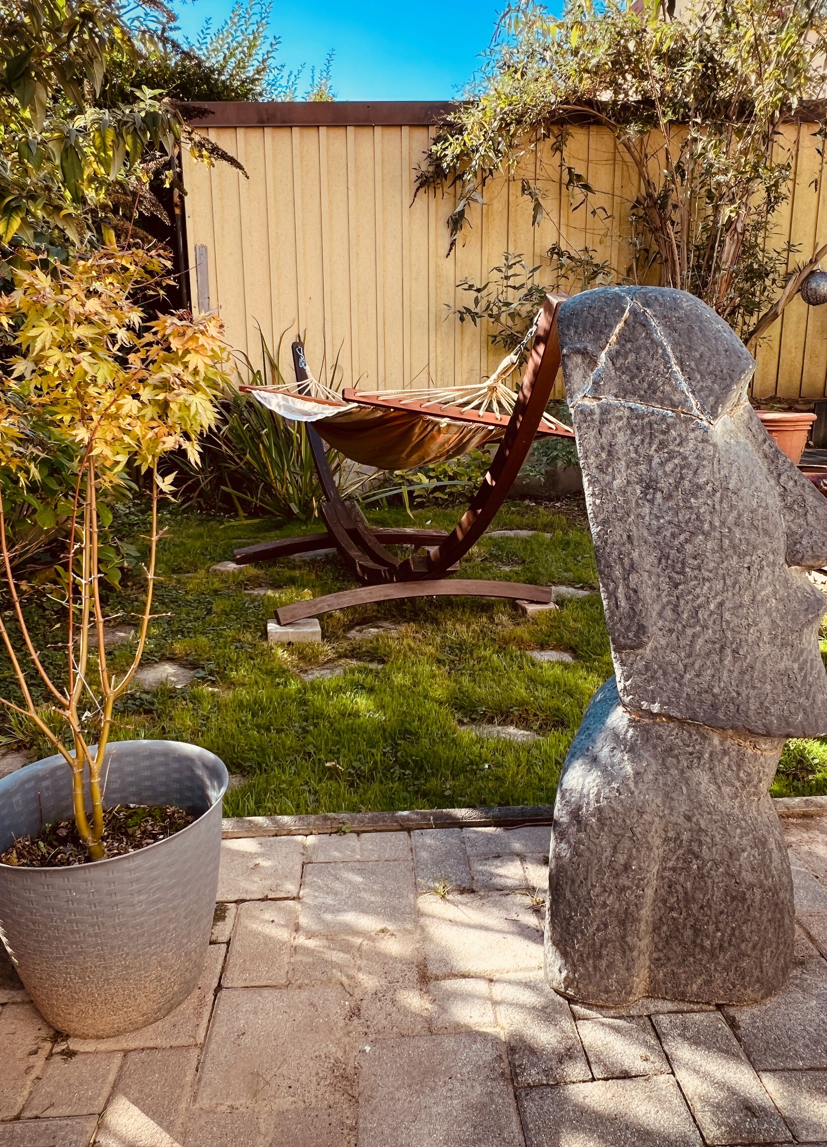 A garden with a hammock, a stone sculpture, and a potted plant.