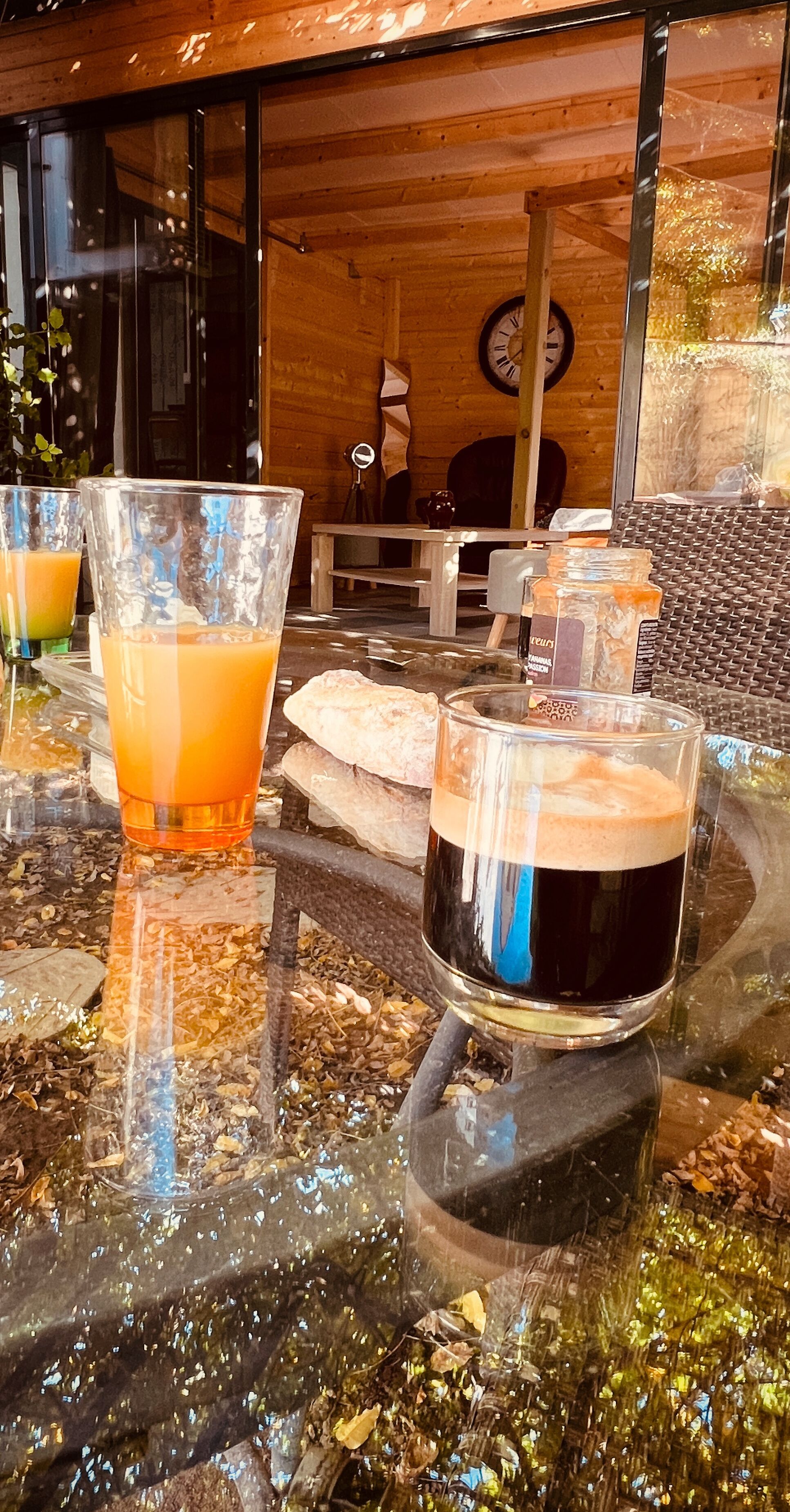 Una taula de vidre amb begudes i una espelma, mobles de fusta i un rellotge a la paret.