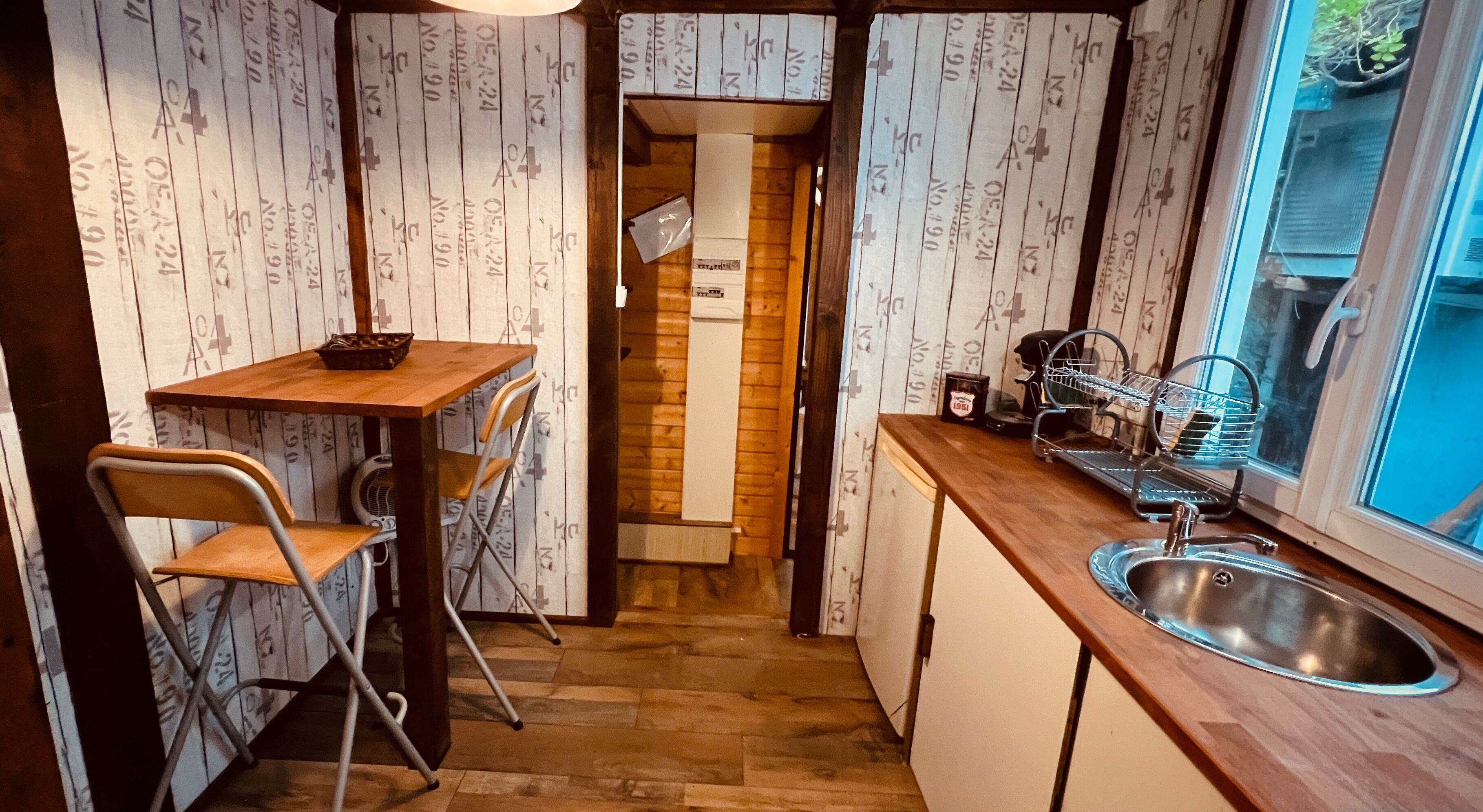Een compacte keuken met houten wanden, een kleine eettafel, twee stoelen, een gootsteen en een raam.