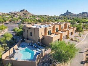 A modern resort with a pool, multiple guest rooms, and a desert landscape in the background.