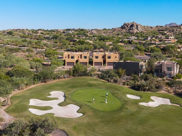 A golf course with bunkers and a building with multiple units in the background.