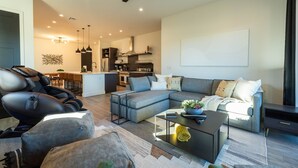 A modern living room with a sectional sofa, a massage chair, a coffee table, and a dining area in the background.