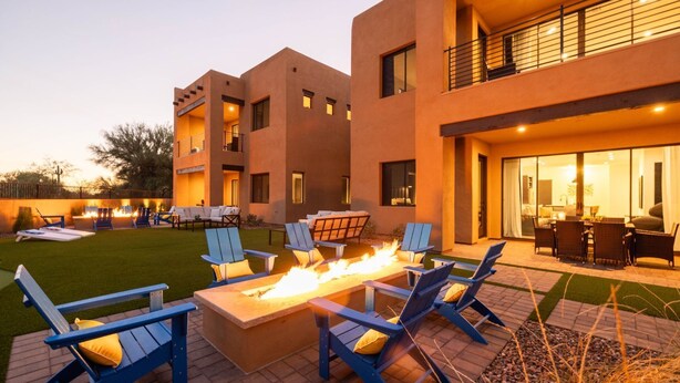A modern outdoor seating area with fire pit and lounge chairs, a well-maintained lawn, and a building with multiple balconies and large windows.