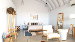 Ein geräumiges Schlafzimmer mit einem großen Bett, einem Holzstuhl, einer Stehlampe und einem Spiegel.