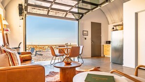 Ein modernes Interieur mit Essbereich, einer Couch, einem runden Tisch und Blick auf die Wüstenlandschaft durch große Fenster.