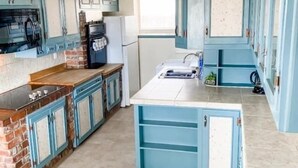 Une cuisine avec des armoires bleues, un mur d’accent en briques, une hotte de cuisinière en acier inoxydable et une horloge numérique affichant le chiffre 140.