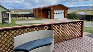 Une cabane en bois avec un garage, une cour clôturée et une terrasse avec une chaise.