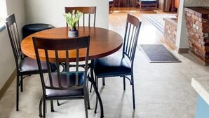 Un coin repas avec une table ronde et des chaises, un élément décoratif mural, et une vue sur un salon doté d’une cheminée.
