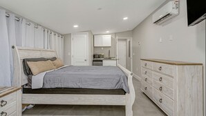 A bedroom with a bed, a dresser, a TV, and an air conditioning unit. - Park Bliss Unit 4. Private Suite
 (Titusville)