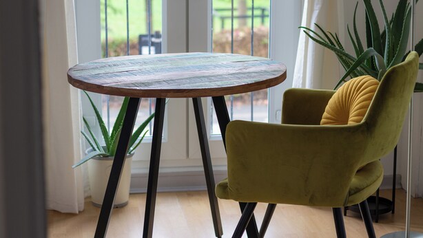 A round wooden table with metal legs, a yellow armchair with a cushion, and a potted plant. - Captivating 3-bed House in London (London)