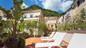 A rooftop terrace with white lounge chairs, potted plants, and terracotta tiles. - Etrus Boutique Room Amalfi (Amalfi)
