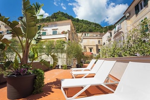 Una terraza en la azotea con sillones blancos, plantas en macetas y baldosas de terracota.