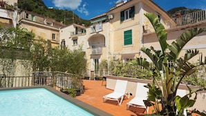 A swimming pool with lounge chairs, surrounded by buildings with balconies and potted plants. - Etrus Boutique Room Amalfi (Amalfi)
