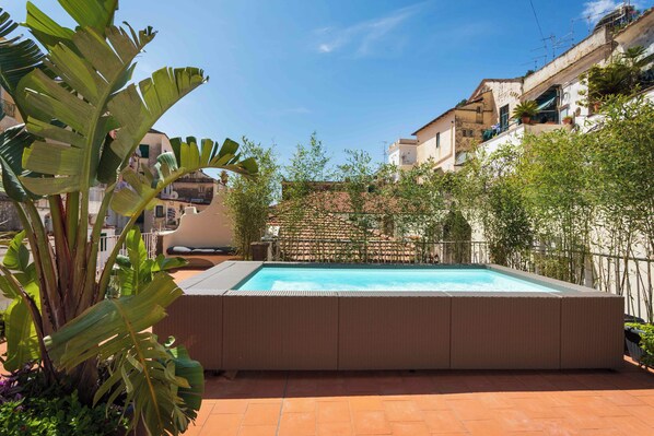 Piscina rectangular con solárium alicatado, rodeada de abundante vegetación y un muro de ladrillo.