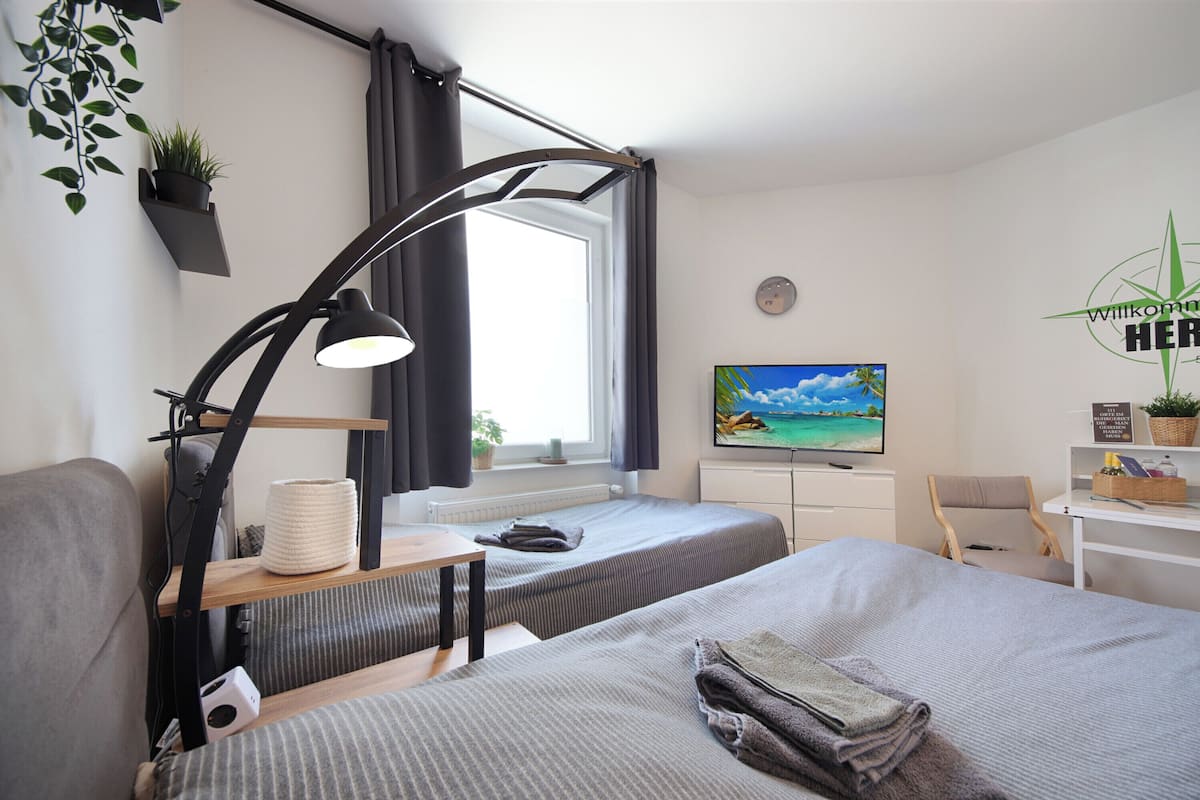 A modern hotel room with two beds, a desk, a TV, and a window with curtains.