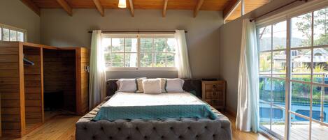 Un dormitorio con una cama grande, techo de madera y vistas al exterior a través de amplios ventanales.