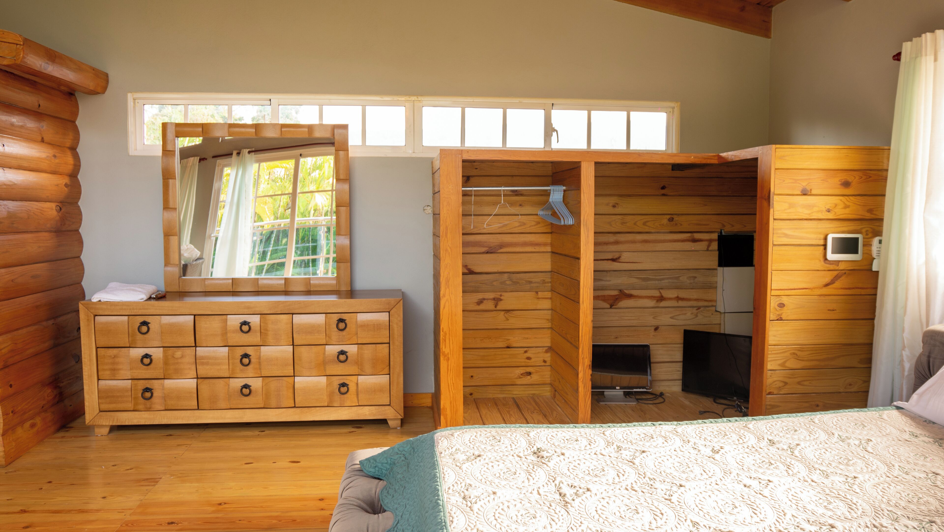 Une chambre située dans une cabane en rondins, avec une commode en bois, un dressing, un lit et une fenêtre avec des rideaux.