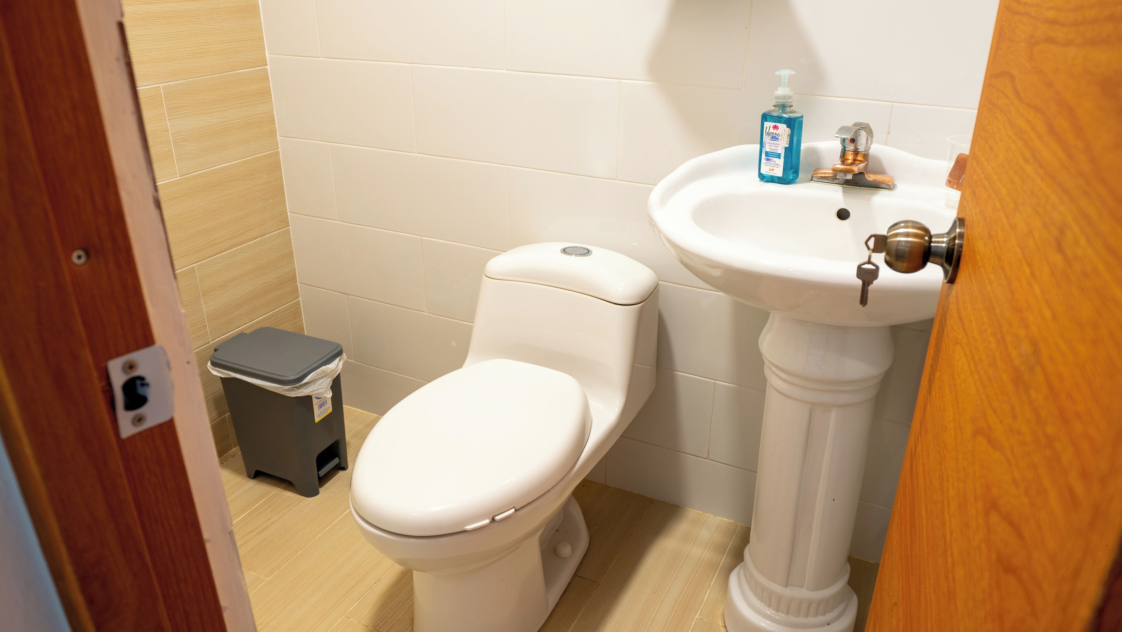 A small bathroom with a toilet, a sink, and a trash bin.
