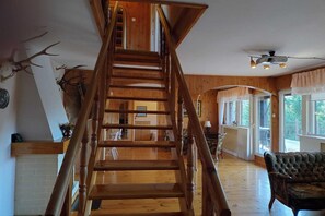 A wooden staircase with a view of the living room below, a fireplace, and a deer head decoration.