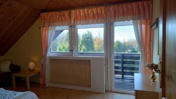 Une pièce avec un plafond en pente, un lit, une petite table avec une lampe, une fenêtre avec des rideaux et une vue sur les arbres à l’extérieur.