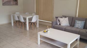 A living room with a white coffee table, a grey sofa, and a dining table with chairs.