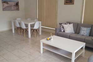A living room with a white coffee table, a grey sofa, and a dining table with chairs. - Victor Central Cottage Perfect Location (Victor Harbor)