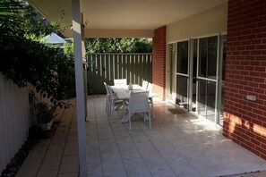 A patio with a table and chairs, a brick wall, and a sliding glass door. - Victor Central Cottage Perfect Location (Victor Harbor)