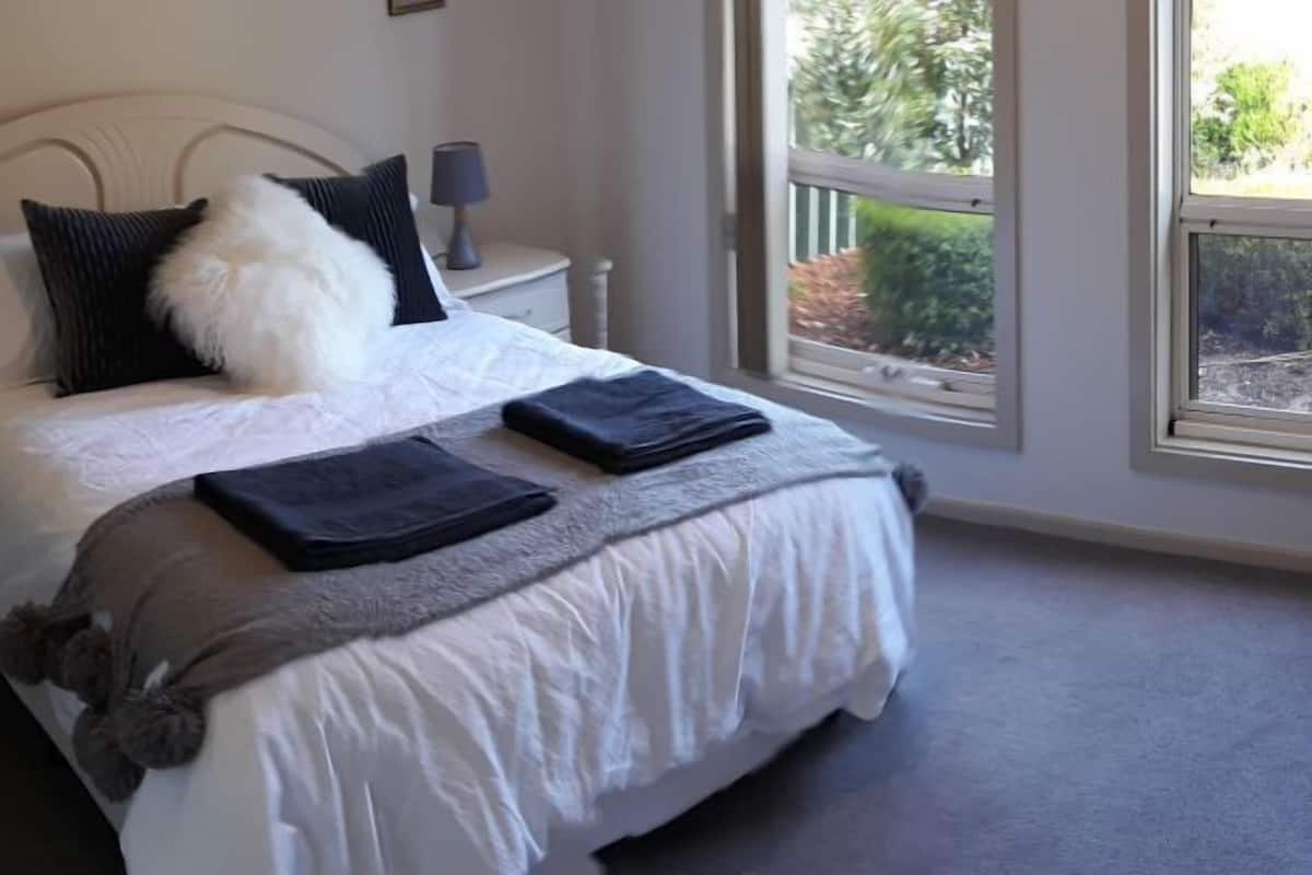 A neatly made bed with a white duvet, grey throw, and a grey blanket. There is a nightstand with a lamp beside the bed.