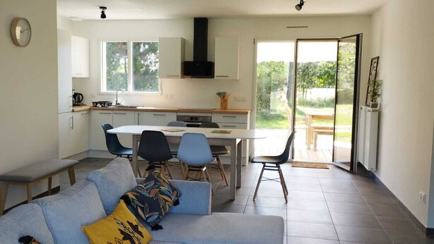 A modern kitchen with a dining area, a sofa with cushions, and a view of the outdoors. - WEST COAST house between ocean, Bassin d'Arcachon, Dune du Pyla, Bordeaux (Le Porge)
