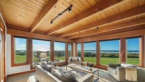 Ein geräumiges Wohnzimmer mit großen Fenstern, einer Holzbalkendecke und modernen Möbeln.