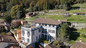 A large, multi-story building with a tiled roof, surrounded by smaller houses and trees.