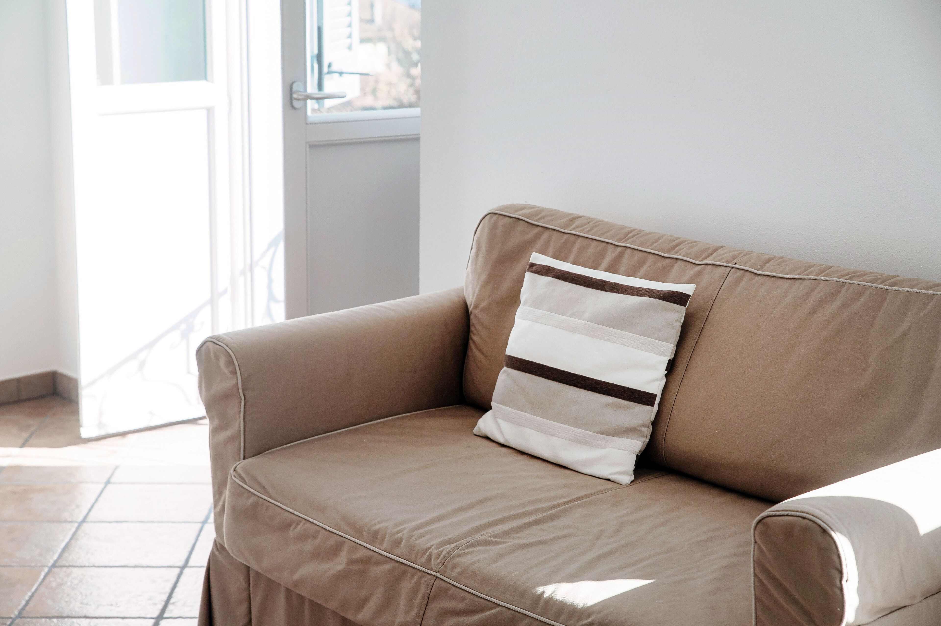 A beige sofa with a striped pillow in a room with a white door and a window.